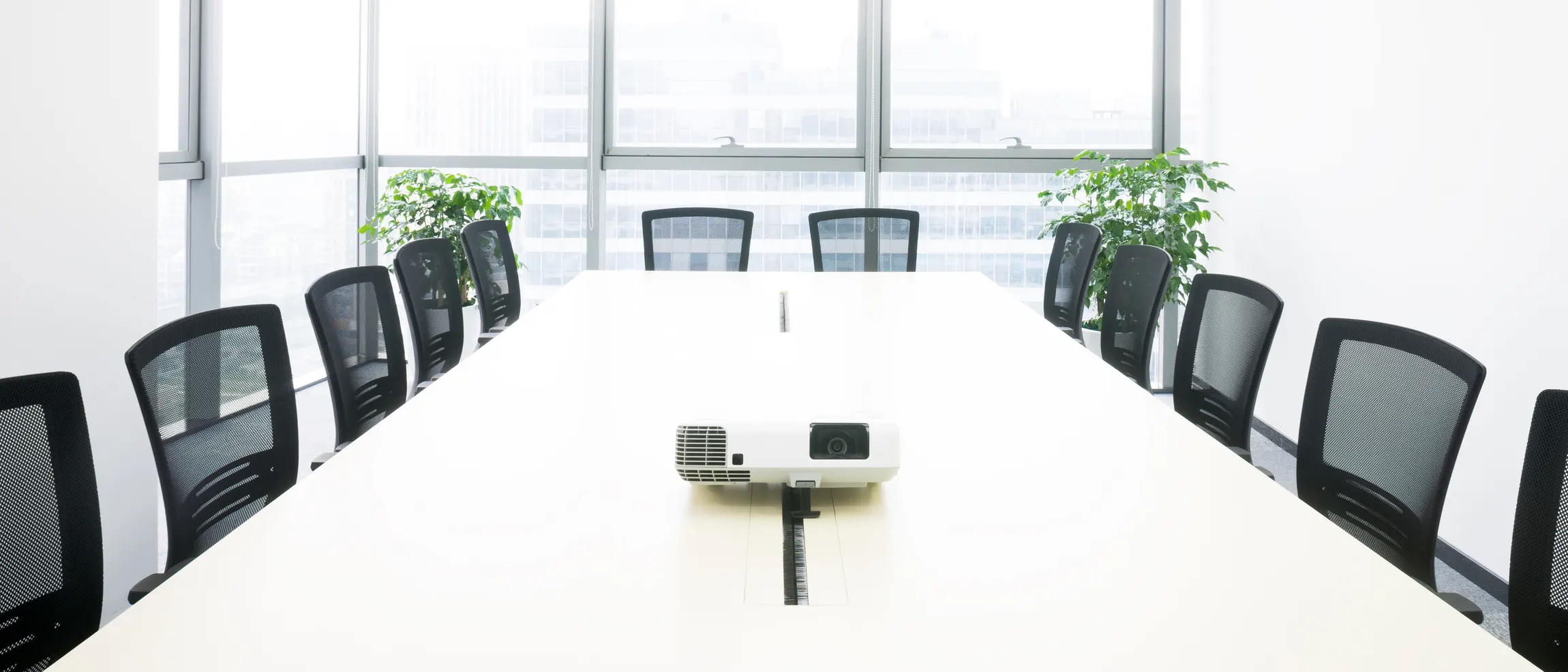 A white boardroom table in a daylit meeting room